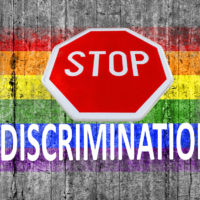 STOP sign and discrimination on top of LGBT flag painted on background STOP sign and discrimination on top of LGBT flag painted on background