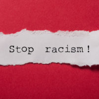 closeup of white torn paper text saying 'stop racism!' on red paper background