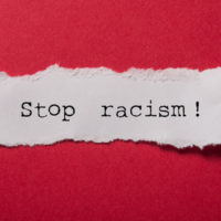 closeup of white torn paper text saying 'stop racism!' on red paper background closeup of white torn paper text saying 'stop racism!' on red paper background