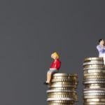 man sits higher on stack of coins than female