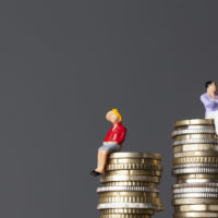 man sits higher on stack of coins than female