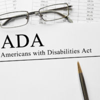 Notepad that reads Americans with Disabilities Act (ADA) on a table with spectacles and pen