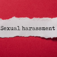 closeup of white torn paper on red paper background with text Sexual harassment