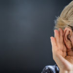 Elderly woman with hearing aid on grey background