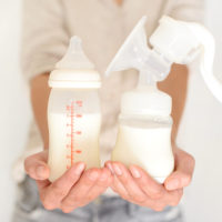 Breast pump and bottle with milk in woman's hand