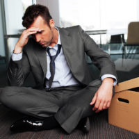 Sad fired businessman sitting with box outside meeting room