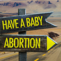 Two different road signs that read have a baby and abortion