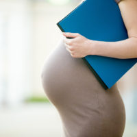 Active pregnancy concept. Close-up of belly of happy young business pregnant woman standing on the street with document folder. Future mom working on her late pregnancy period