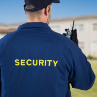 Rear view of security guard using radio against house
