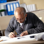 Senior architect working on construction blueprint in office, he draws with a pencil and ruler.