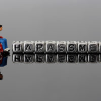 Miniature scale model man in a wheelchair with the word harassment on beads reflected on a dark background