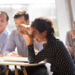 Indian woman laughing eating pizza with diverse coworkers in office