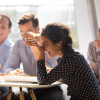 Indian woman laughing eating pizza with diverse coworkers in office