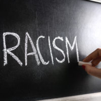 Hand writing the word racism on blackboard. Stop hate. Against prejudice and violence. Lecture about discrimination or stereotypes in school.