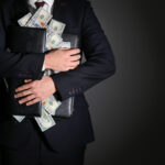 Businessman holding briefcase with dollar banknotes on dark background. Corruption concept