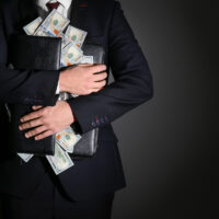 Businessman holding briefcase with dollar banknotes on dark background. Corruption concept