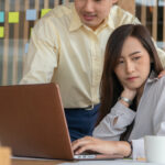 Businessman putting hand on the shoulder of female employee in office at work. She unhappy and feeling displeased with inappropriate actions his boss. Concept of sexual harassment in workplace