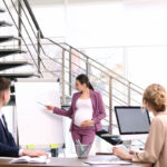 Young pregnant woman giving presentation to colleagues at workplace