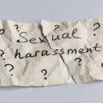 Sexual harassment concept. A torn piece of crumpled paper with many question mark signs and the words sexual harassment