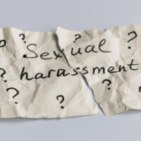 Sexual harassment concept. A torn piece of crumpled paper with many question mark signs and the words sexual harassment