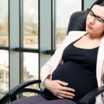Tired  beautiful pregnant woman sitting at workplace in the office