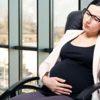 Tired  beautiful pregnant woman sitting at workplace in the office