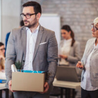 Fired male employee holding box of belongings in an office Fired male employee holding box of belongings in an office