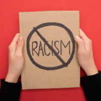 cropped view of woman holding carton placard with stop racism sign on red background cropped view of woman holding carton placard with stop racism sign on red background
