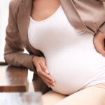 Young pregnant woman in suit at workplace, closeup