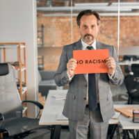 Serious man standing in office and holding no racism placard