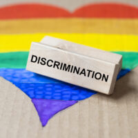 Discrimination word on wooden block on lgbtq flag in heart Discrimination word on wooden block on lgbtq flag in heart