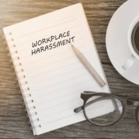 Workplace harassment concept on notebook with glasses, pencil and coffee cup on wooden table. Business concept. Workplace harassment concept on notebook with glasses, pencil and coffee cup on wooden table. Business concept.