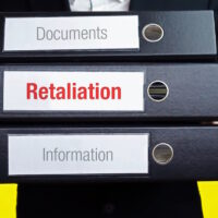 Retaliation. Man carries stack of folders. File folders with text label. Background yellow.