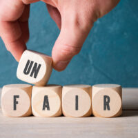 Hand verändert Wort "unfair" zu "fair" durch Wegnahme eines Würfels