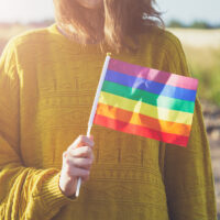 young woman wearing yellow sweater holding lgbt rainbow flag outside, same sex couples, freedom, love, equal rights concept