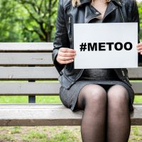 Hashtag for Mee Too movement Woman sitting on a bench at the park with a broadsheet againts sexual harassment Hashtag for Mee Too movement Woman sitting on a bench at the park with a broadsheet againts sexual harassment