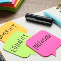 Sticky notes with words Diversity, Equality, Inclusion and stationery on wooden table, closeup