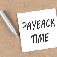PAYBACK TIME text on sticky note on a cork board with pencil ,