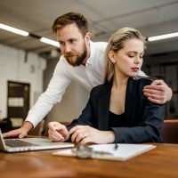 A bearded male Manager harasses his colleague a girl who works at a laptop in the office A bearded male Manager harasses his colleague a girl who works at a laptop in the office