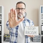 Middle age man business worker holding stop racism notebook at office