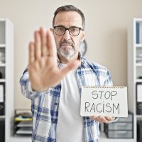 Middle age man business worker holding stop racism notebook at office Middle age man business worker holding stop racism notebook at office