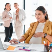 Gossip, pregnancy shame or business people pointing at pregnant woman in office working on laptop. Colleagues in workplace bullying, employee victim exclusion or worker harassment and discrimination