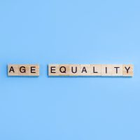 Words Age Equality. Wooden blocks with letters on blue background. Age discrimination concept. Copy space.