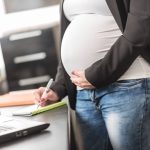 Pregnant woman standing and taking notes at office
