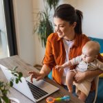 Shot of a young woman working on laptop while caring for her adorable baby girl at home.