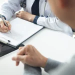 Doctor and patient at hospital office. Doctor working on diagnostic examination on men's health disease and writing on prescription record information document at medical clinic, close up
